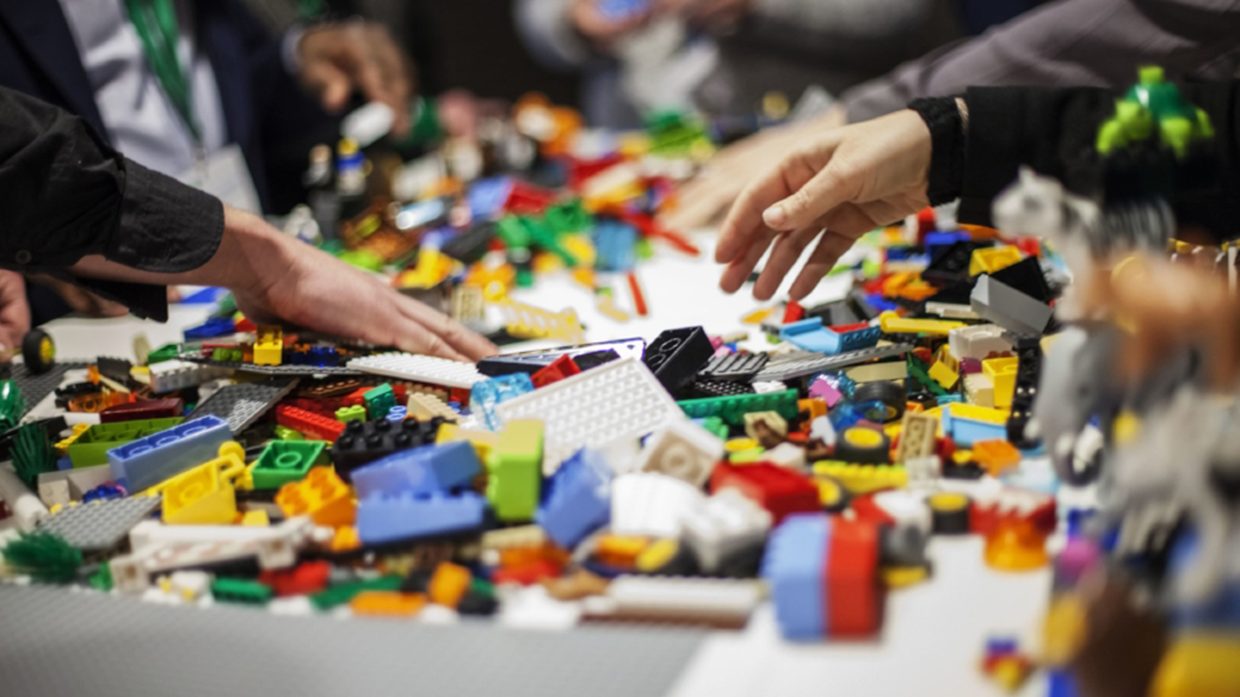 Des mains autour d'une table couverte de briques LEGO lors d'un atelier d'équipe